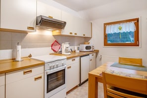 A compact kitchen with a stove, microwave, and a window with a curtain.