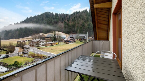 A balcony with a view of a village, a wooden table, and a chair. - Apartment 'Haus Johanna' with Mountain View, Balcony and Wi-Fi (Todtmoos)