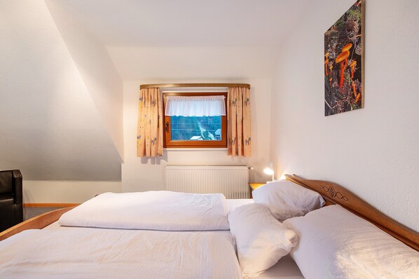 A bedroom with a bed, a window with curtains, a radiator, and a painting on the wall.
