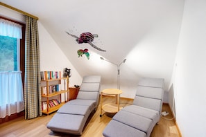 A room with two grey sofas, a bookshelf, a ceiling mural, and a window with curtains.