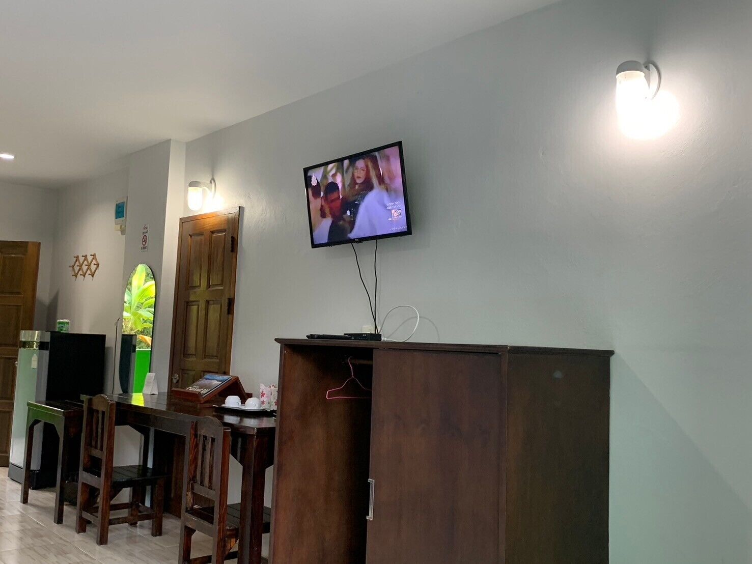 Um saguão de hotel com uma mesa de recepção, uma televisão fixada na parede e uma cadeira de madeira.