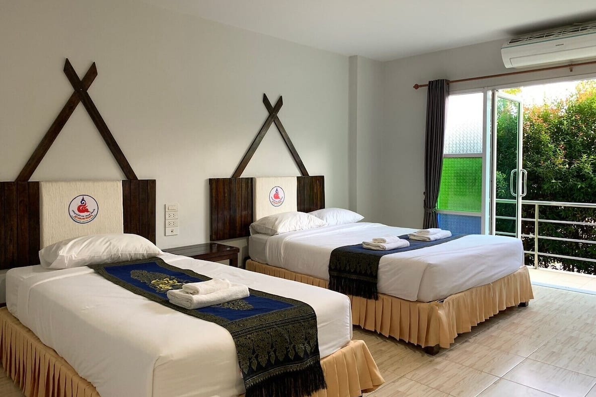 A hotel room with two beds, a balcony with a view, and an air conditioning unit.