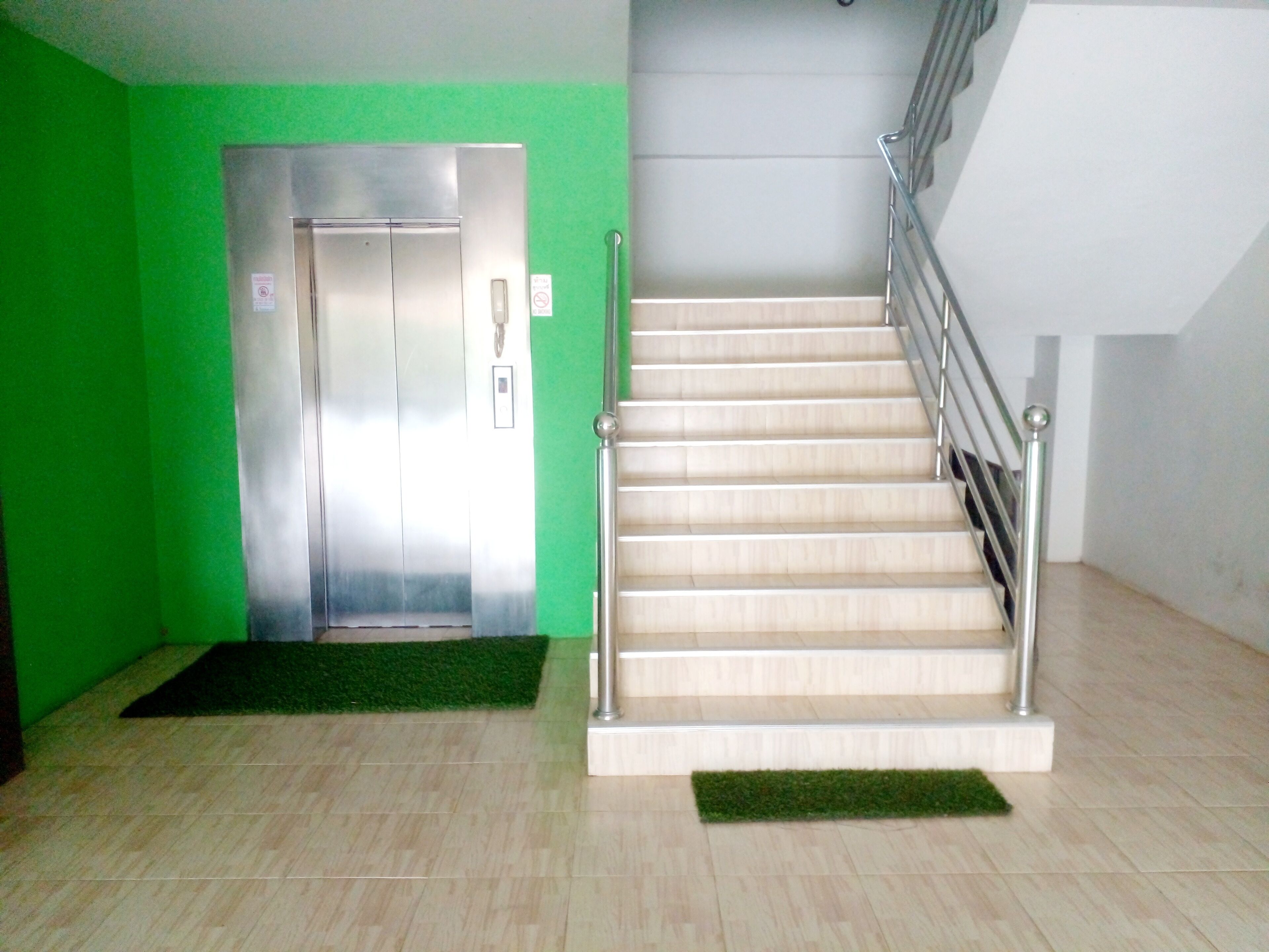 A staircase with a metal handrail and a green carpet at the base.