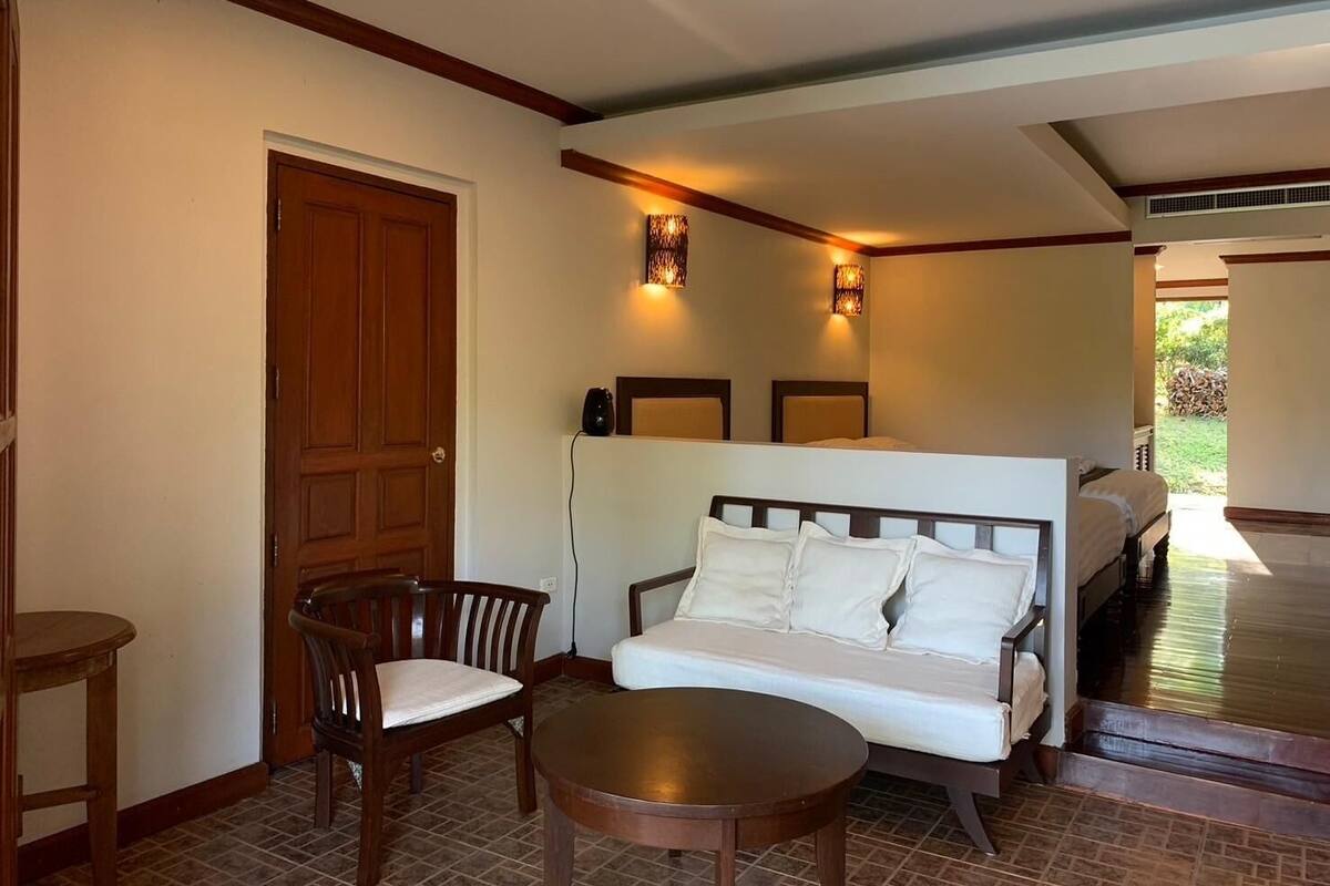 A room with a bed, a sofa, a chair, a table, and a door.