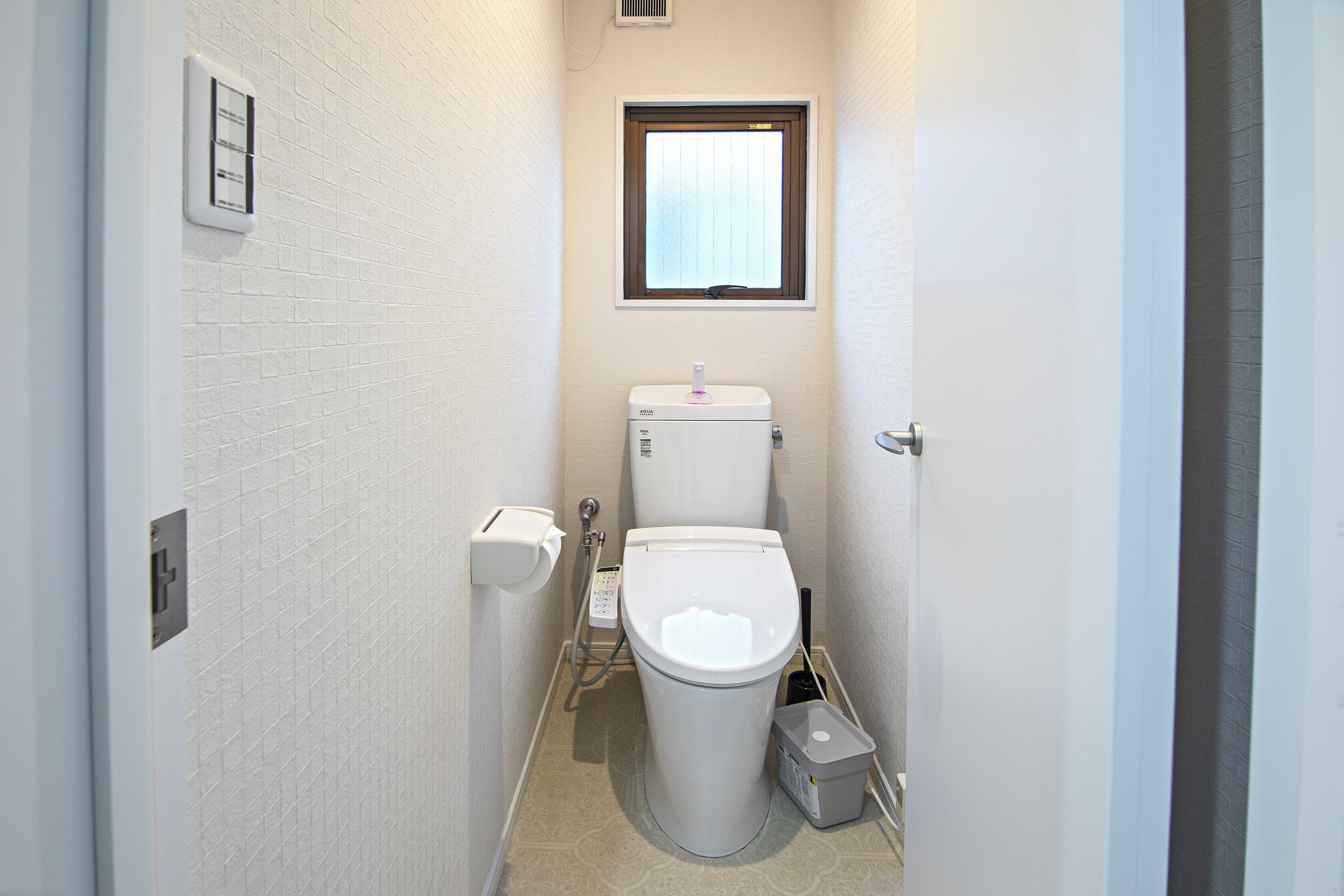 Een kleine, smalle badkamer met toilet, een raam en een prullenbak.