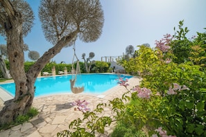 A swimming pool with a stone deck, surrounded by greenery and trees.