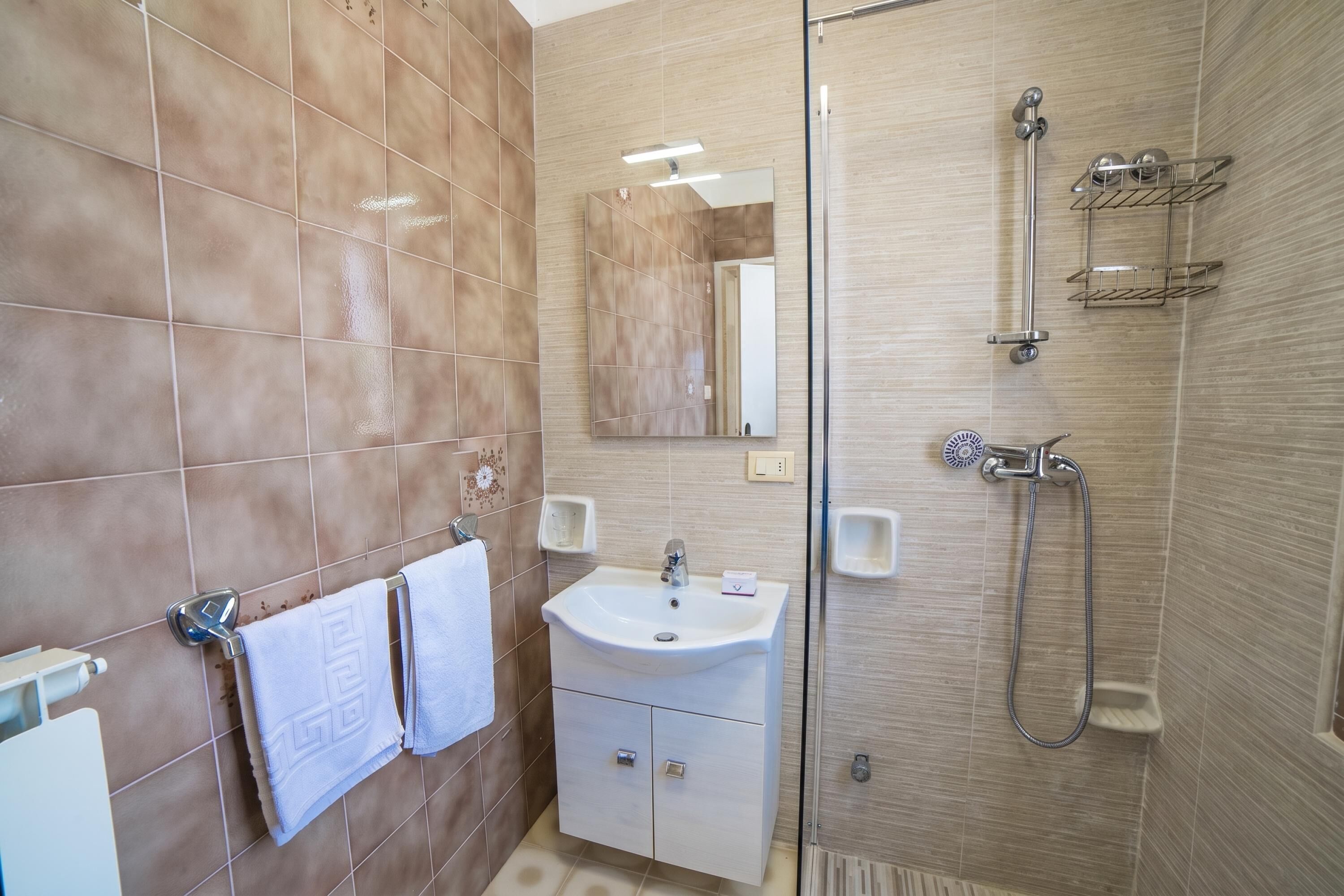A bathroom with a sink, mirror, towel rack, shower, and tiled walls.