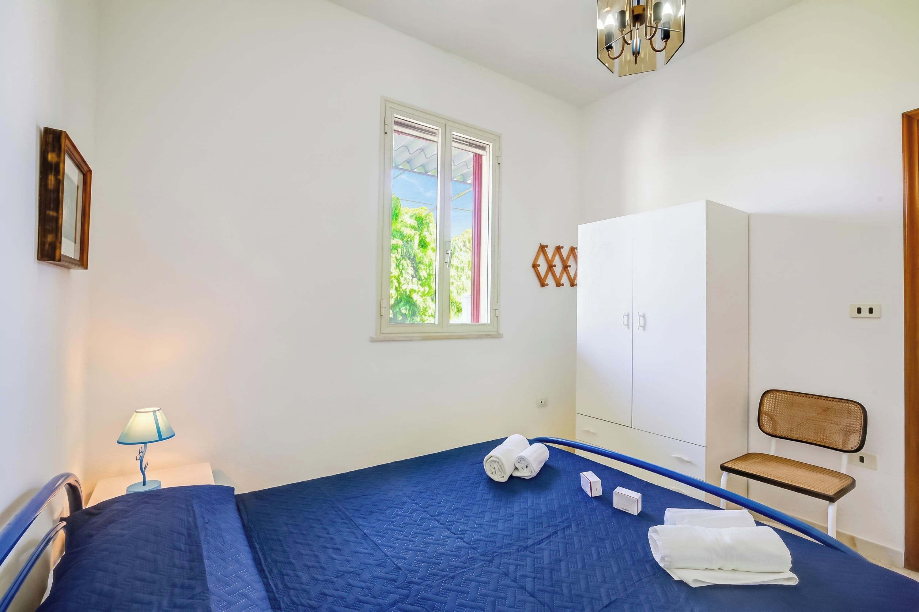 A bedroom with a bed, a window, a wardrobe, a chair, and a lamp.