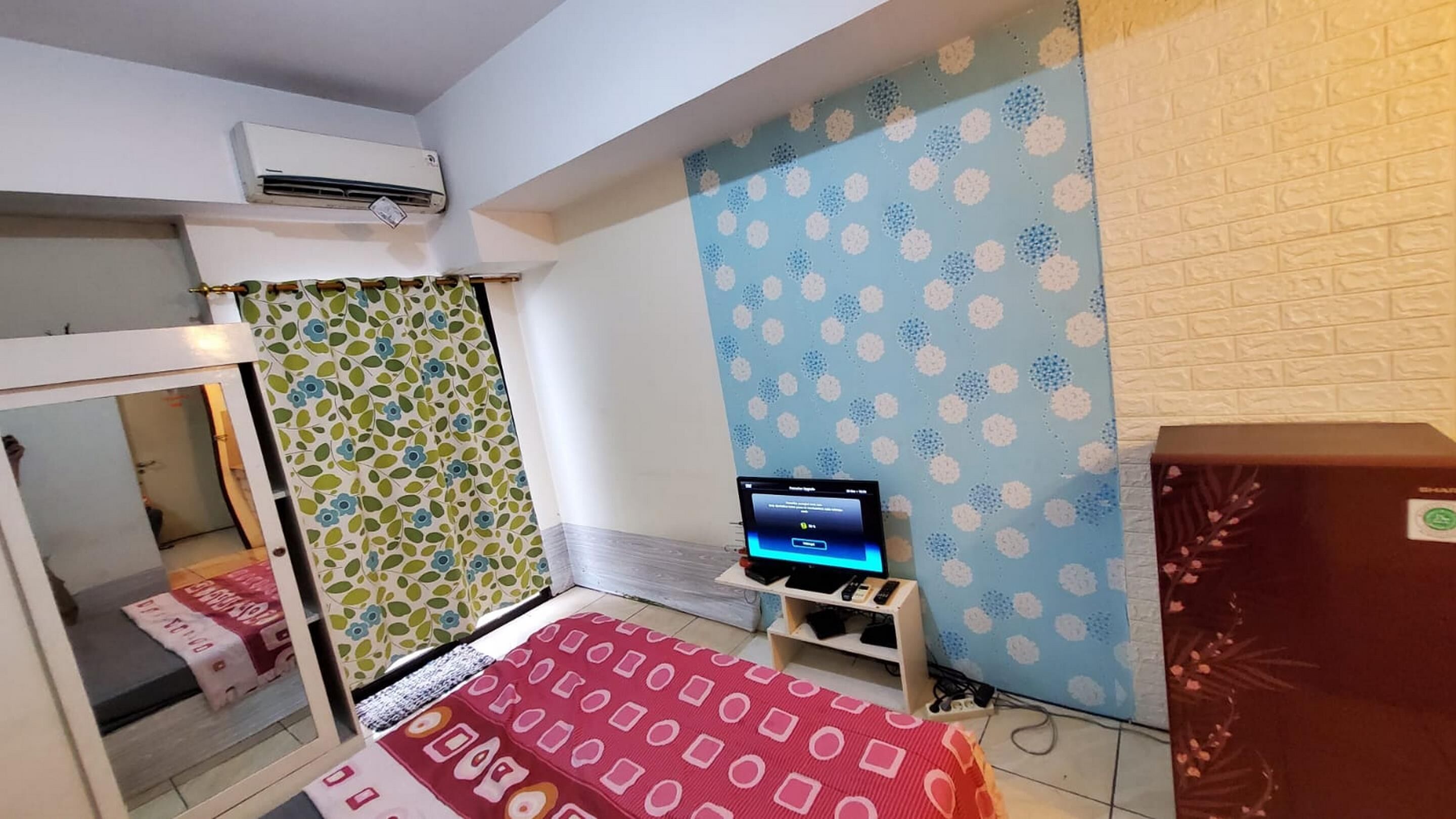 Habitación de hotel pequeña con cama, un escritorio y computadora portátil, aire acondicionado y pared con diseño.