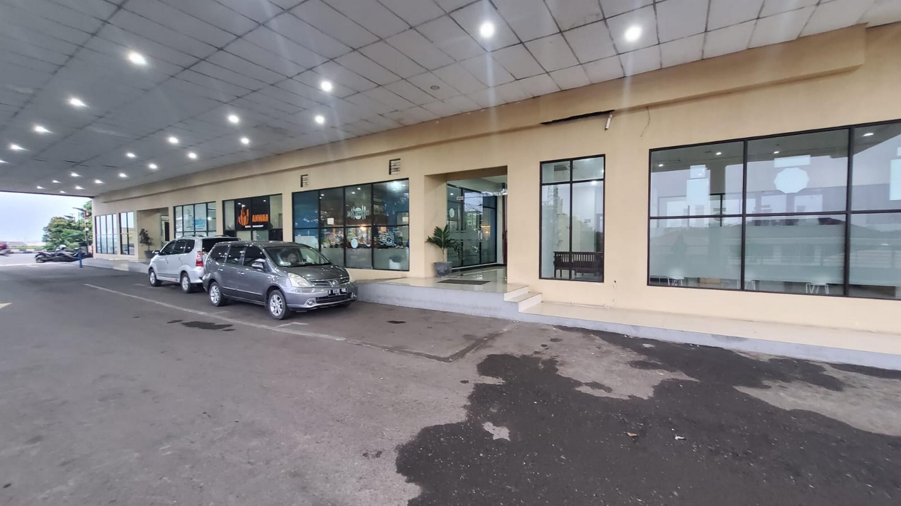 Un edificio con techo plano, amplias ventanas y un estacionamiento lleno de coches.