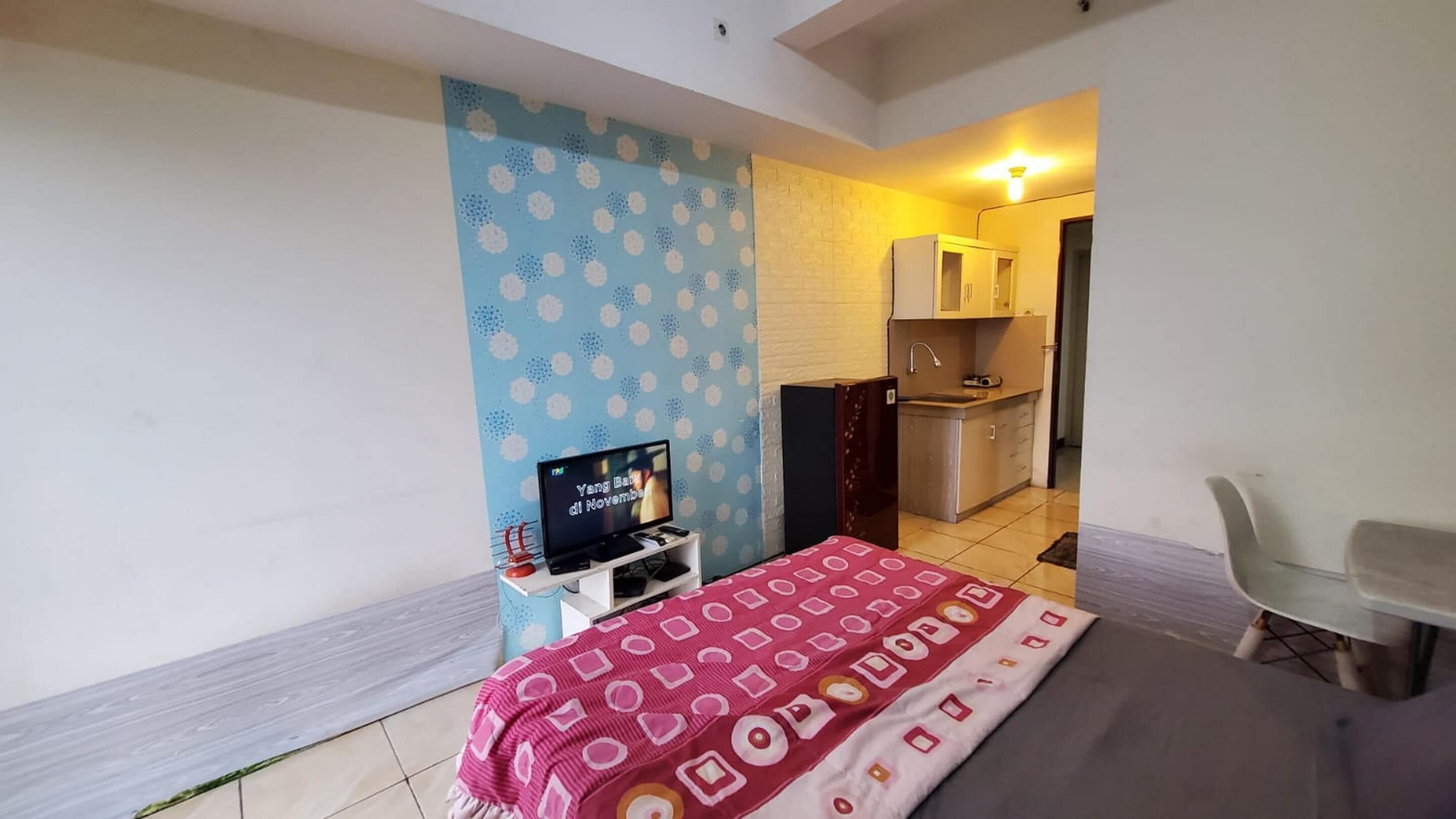 Une petite pièce, de taille modeste, comprenant un lit, un téléviseur, un bureau et une kitchenette.