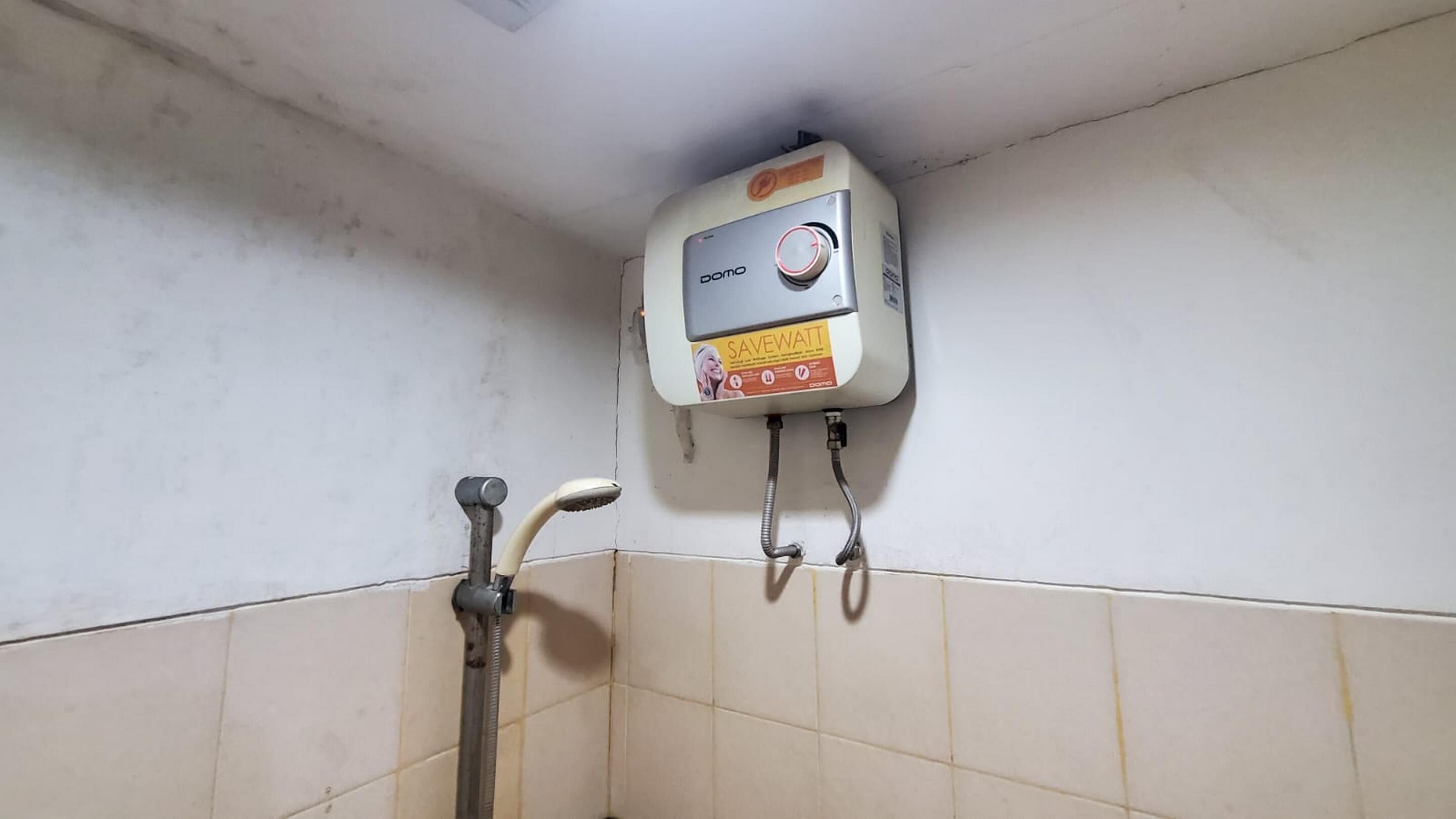 A bathroom with a wall-mounted water heater, a showerhead, and a visible water pipe.