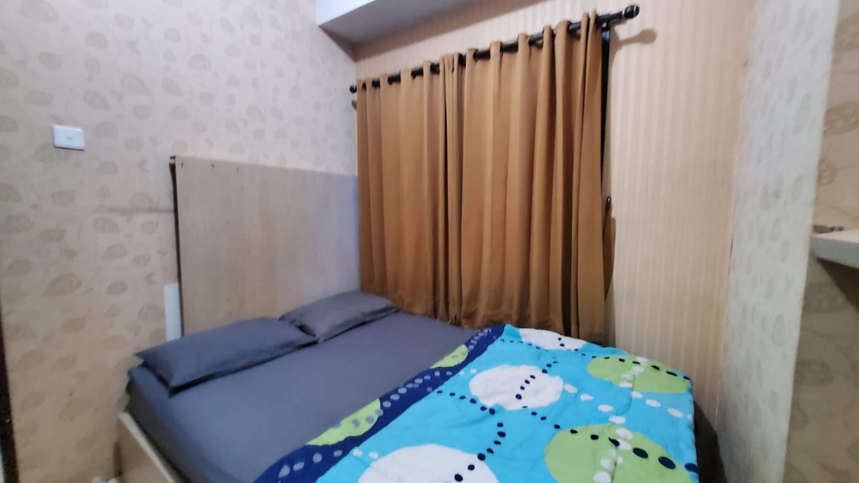 A small room with a bed, a window with curtains, and a patterned wall.