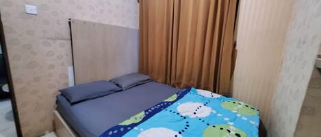 Una habitación pequeña con una cama individual, un cabecero sencillo, una pared con estampado y una ventana con cortinas marrones.