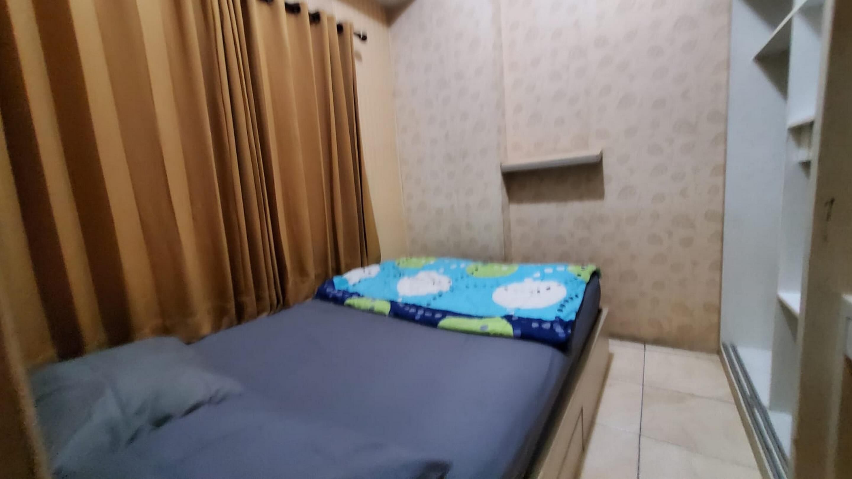 A small, single-bed room with a plain wall and a shelf unit.