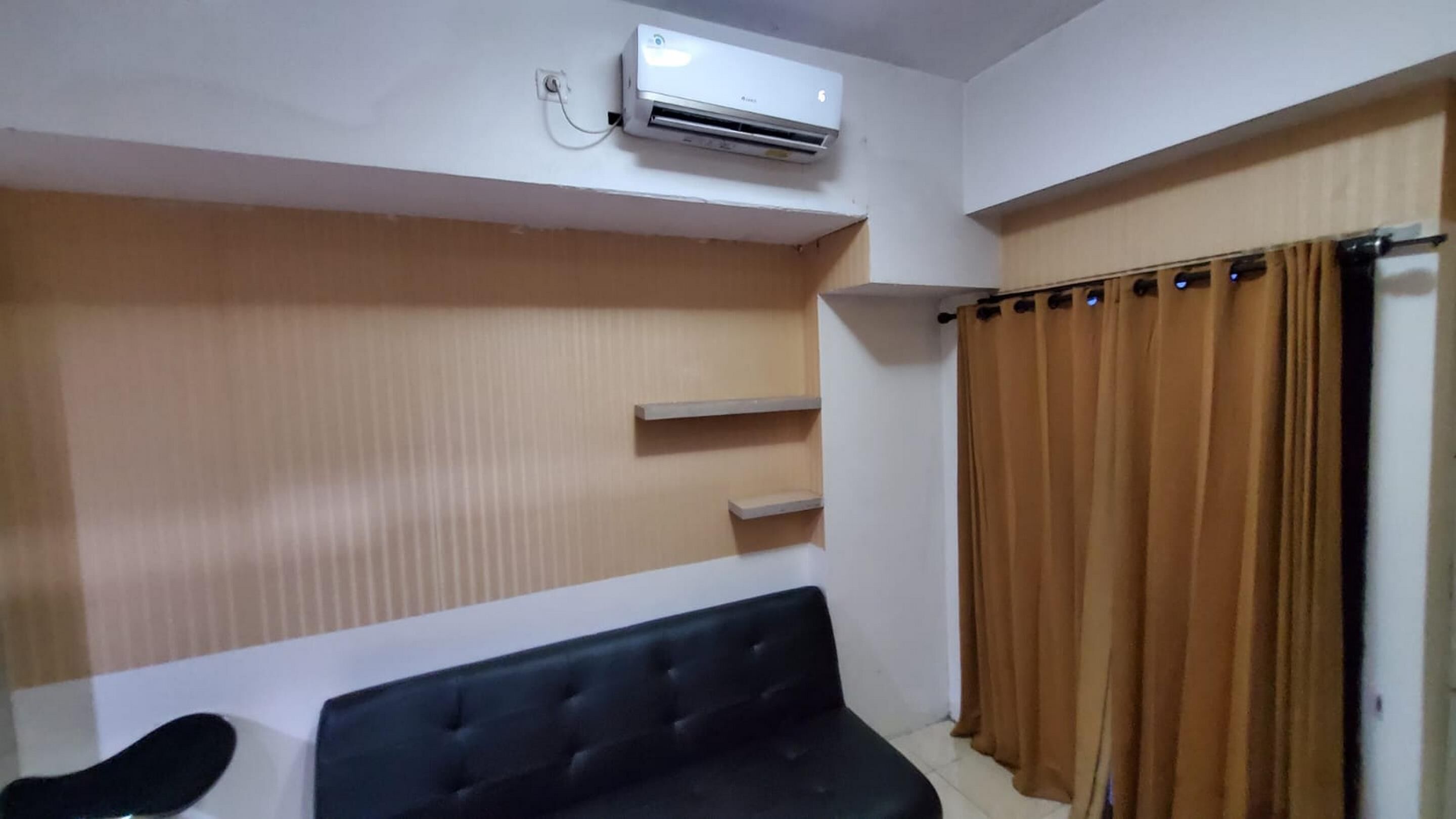 Una habitación con sofá negro, aire acondicionado instalado en la pared y ventana con cortinas marrones.