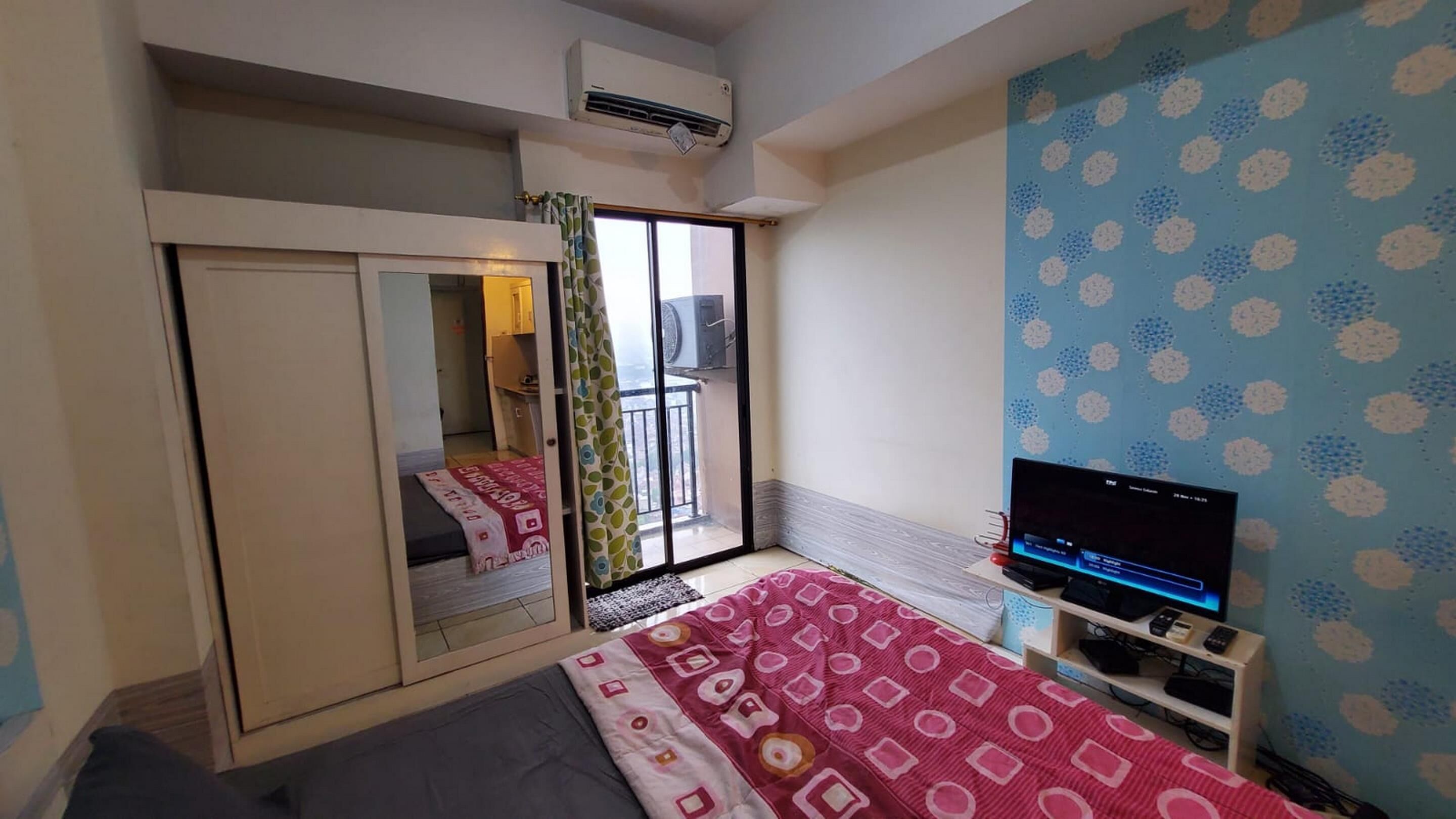 A bedroom with a bed, a TV, a wardrobe, and a balcony with a view.
