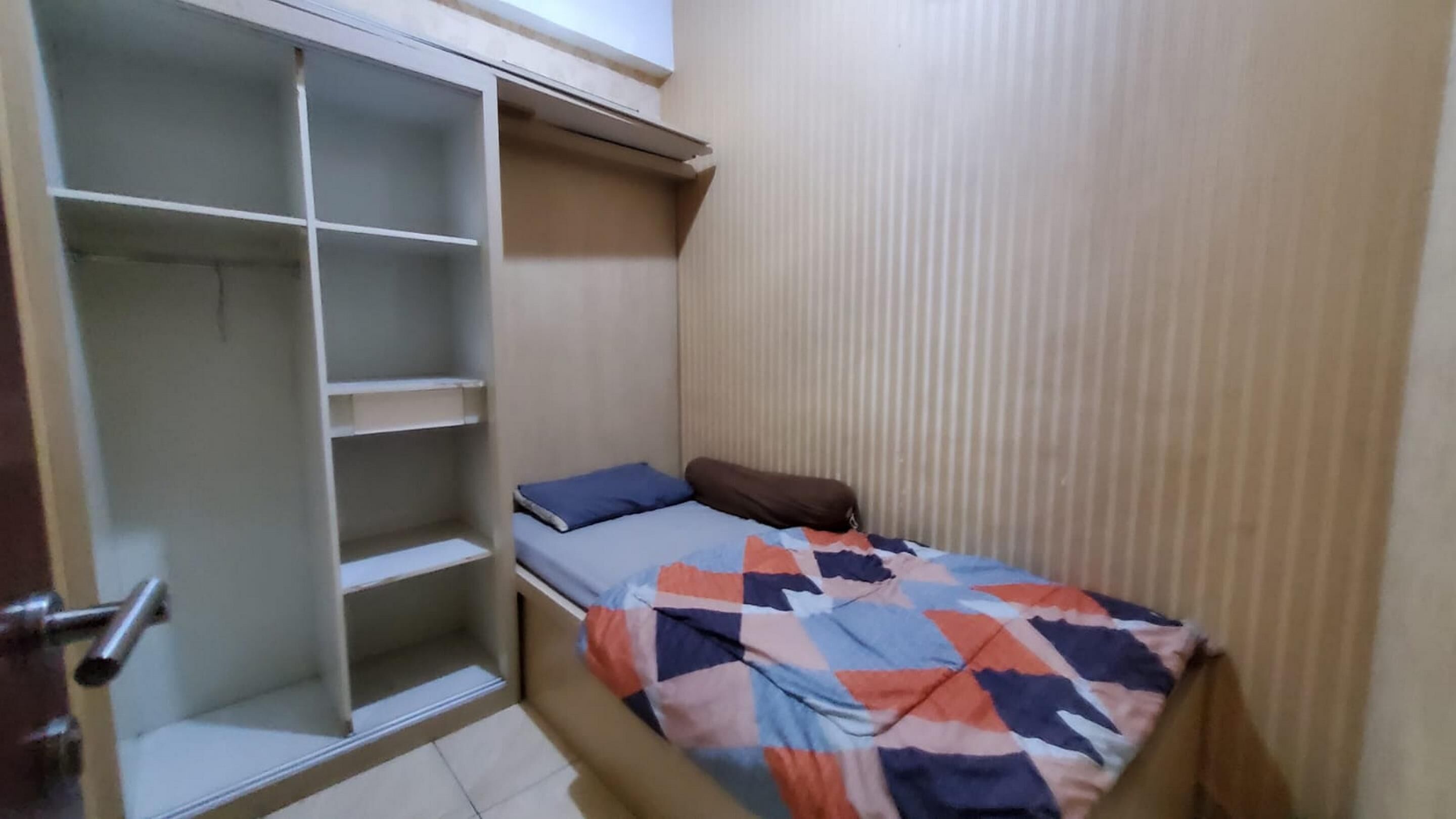 A small, compact room with a bed, a wardrobe, and a door.