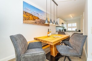 A dining area with a wooden table and four grey upholstered chairs, a bottle of wine, and a magazine on the table.