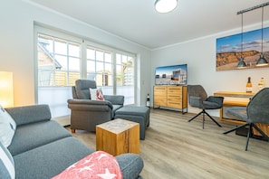 Een moderne woonkamer met grijze banken, een houten salontafel en een televisie op een houten kast.