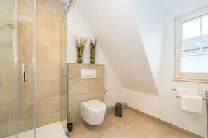 A modern bathroom with a glass shower enclosure, a white toilet, and a window providing natural light.