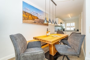Un coin repas avec une table en bois et quatre chaises grises à revêtement rembourré, une bouteille de vin et un magazine posés sur la table.