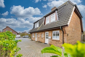 Une maison à deux étages, construite en briques, avec un toit en pente, une porte d’entrée et un garage.
