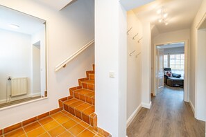 Een trap met oranje tegels, een witte radiator en een spiegel. Een gang met houten vloer en een deur die leidt naar een kamer met een bank en een raam.