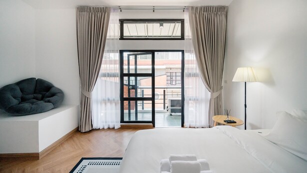 Een hotelkamer met een bed, een zithoek, een lamp en uitzicht door een glazen deur.