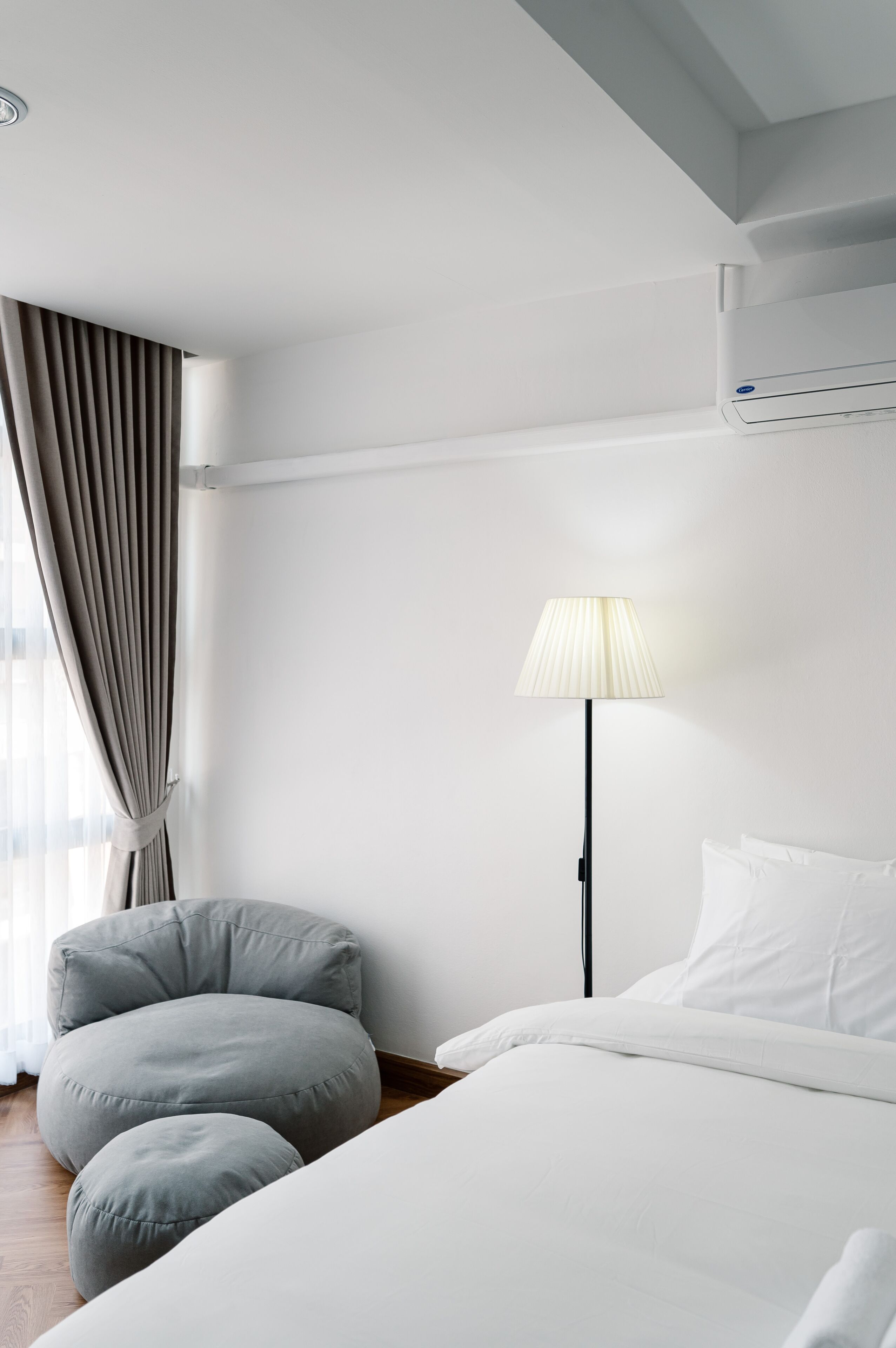 Une chambre d’hôtel moderne avec un lit, un fauteuil gris, une lampe sur pied et une fenêtre avec des rideaux.