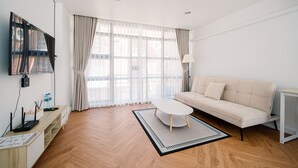 Een moderne woonkamer met een bank, salontafel, televisie en bureau met een lamp.