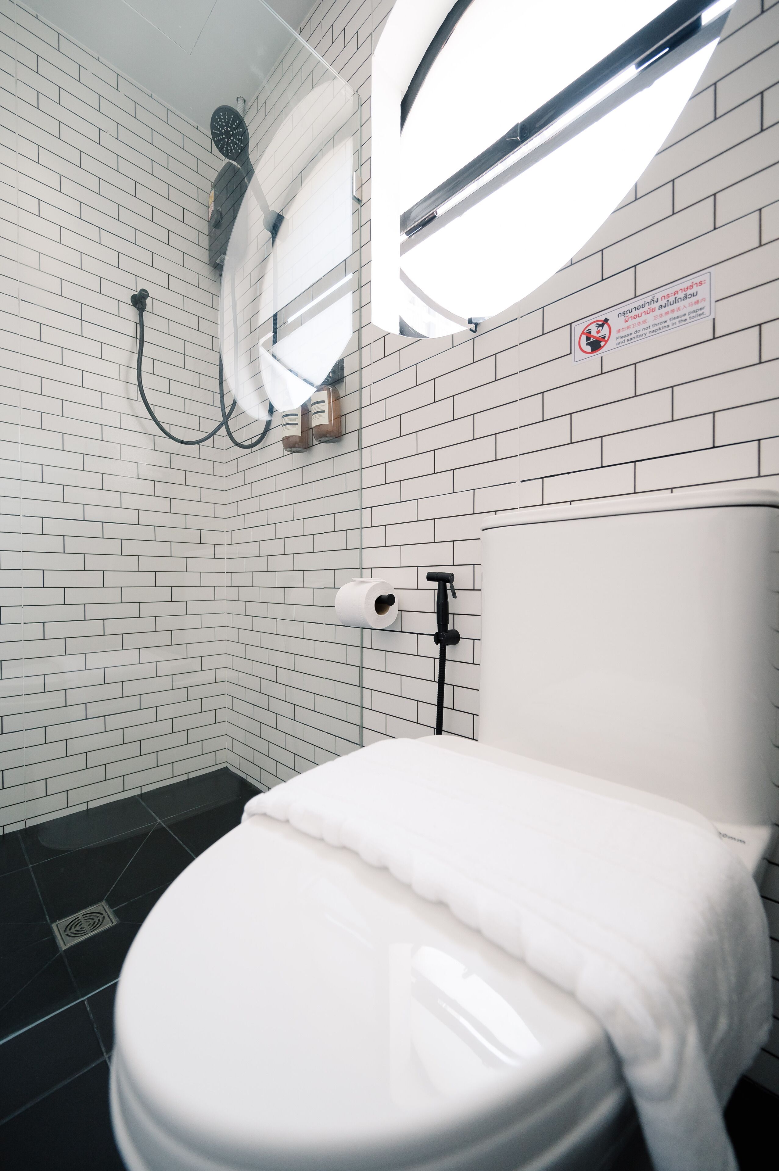 A modern bathroom with white tiled walls, a white toilet, a shower head, and a toilet paper holder.