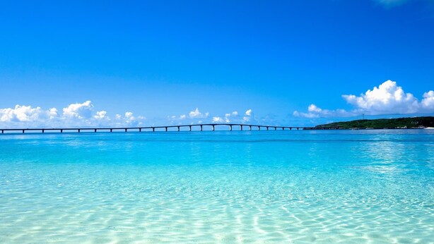 Un mar azul y transparente con un puente a lo lejos.