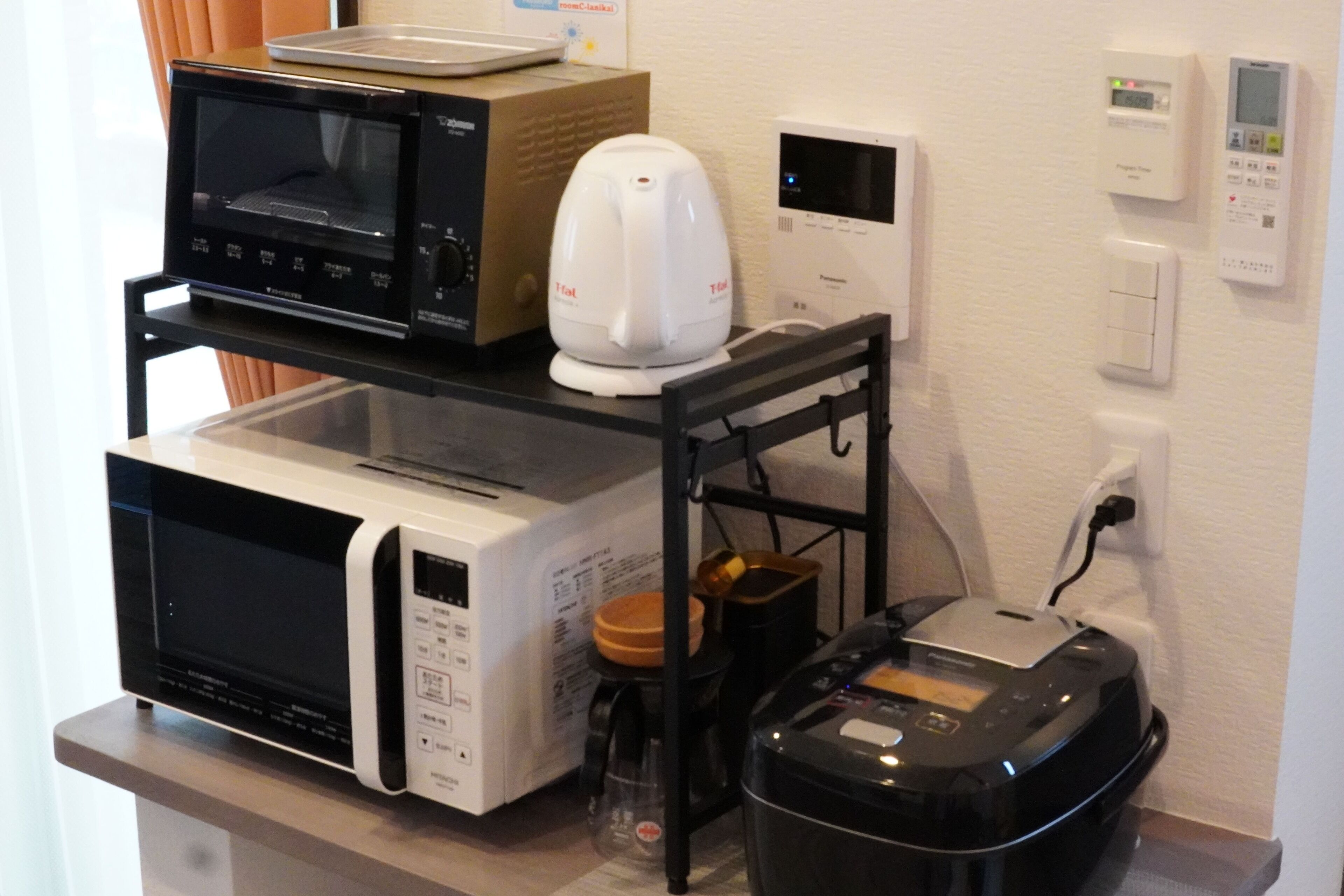 A kitchen with a microwave, toaster, and coffee maker on a shelf, and a trash bin below.