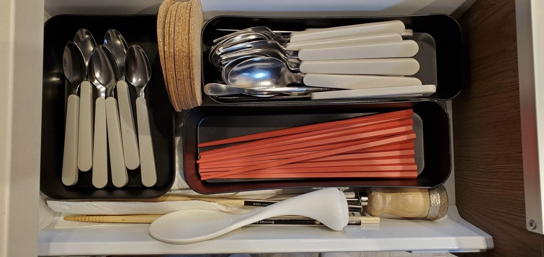 Un tiroir contenant divers ustensiles, notamment des cuillères, des baguettes et une spatule à riz.