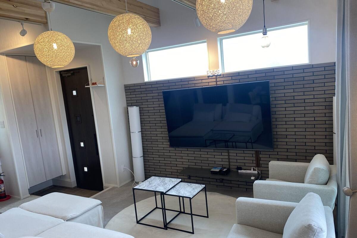 A modern living room with a large flat-screen TV, white sofas, a marble coffee table, and three spherical pendant lights.