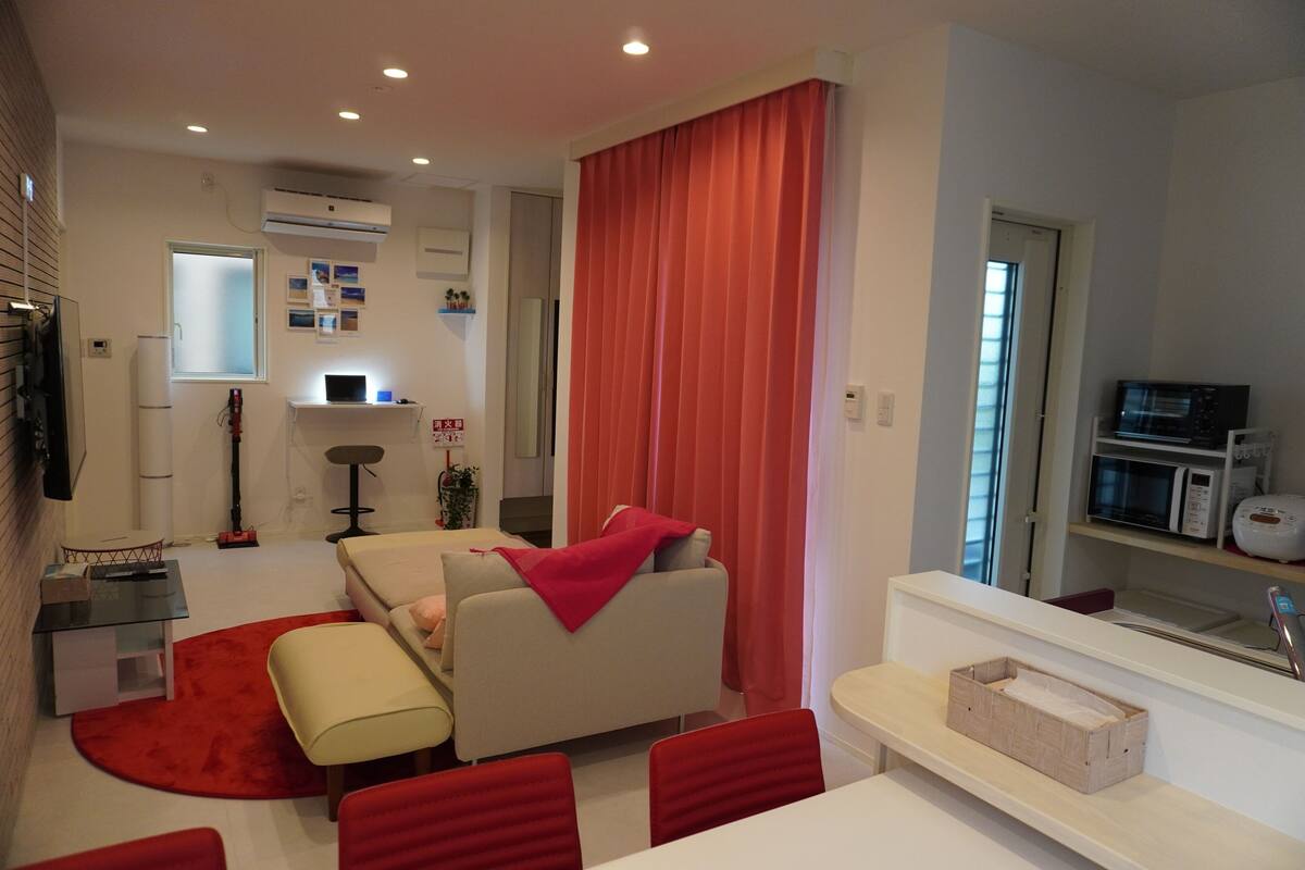 A modern living room with a sofa, red chairs, a dining table, and a kitchen area with a microwave.