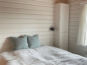 Cozy retreat with a comfortable bed, a wardrobe, and a window with white curtains.