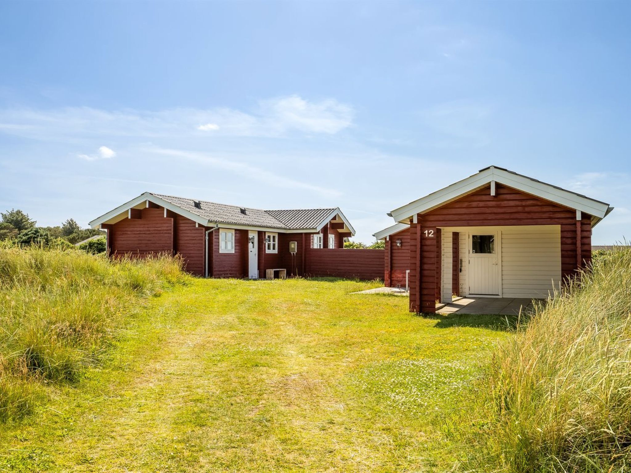 A two-story wooden house with a garage, surrounded by tall grass and a clear sky.