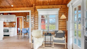 L’intérieur d’une cabane en rondins comprend une cuisine, un coin repas et un espace détente avec vue sur l’extérieur.
