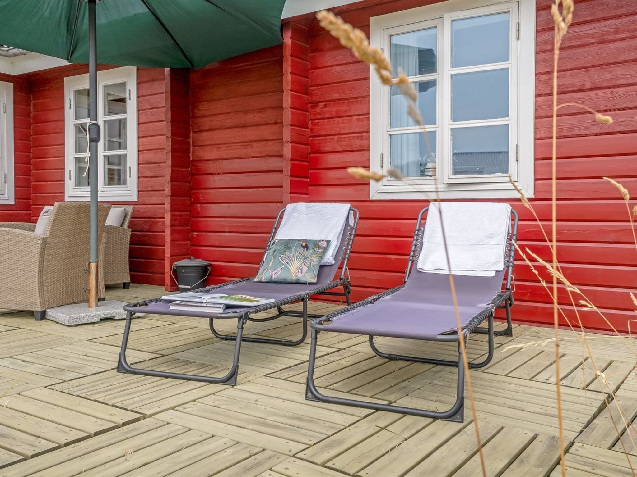 Une maison en bois rouge avec deux fauteuils de jardin sur une terrasse en bois.