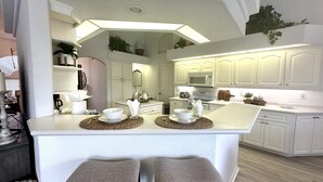Une cuisine moderne avec des meubles blancs, un îlot central doté de tabourets et un four à micro-ondes placé au-dessus du plan de travail.