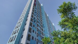 A tall, modern high-rise building with a prominent red and white logo on the top. - OYO Life 92889 Apartement Grand Sentraland Karawang By A.t Room (Karawang)