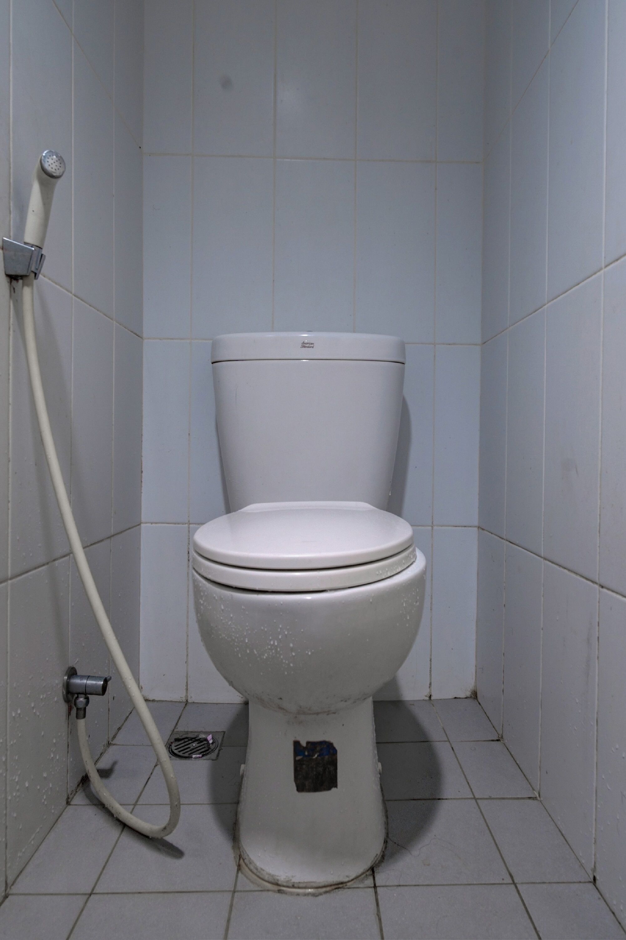 A white toilet in a small, tiled bathroom with a visible water pipe on the left.