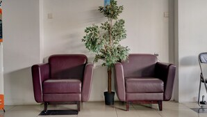 Two leather armchairs, a potted plant, and a vacuum cleaner in a room with tiled flooring and a plain wall. - OYO Life 92889 Apartement Grand Sentraland Karawang By A.t Room (Karawang)
