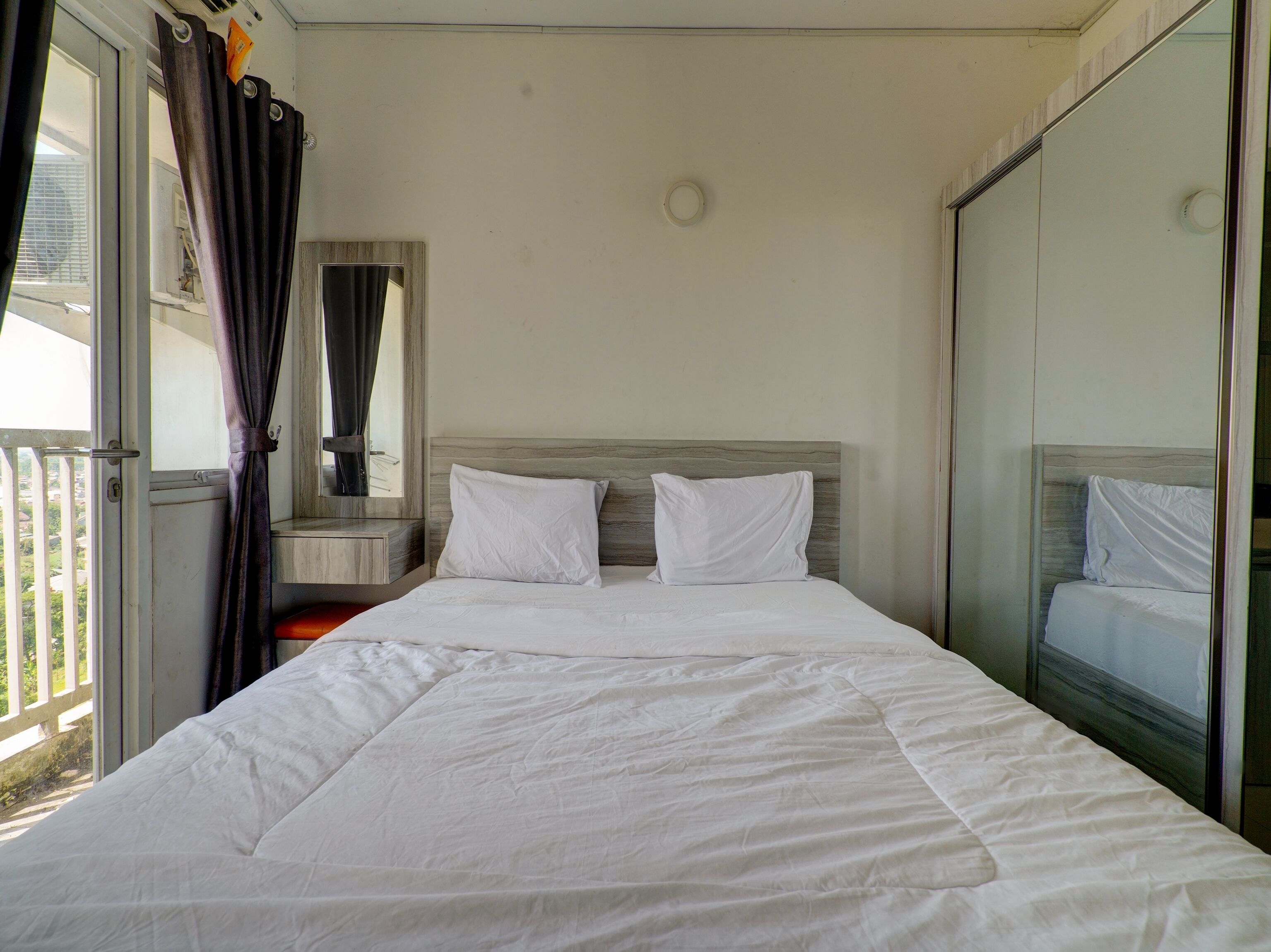 A single-bed room with a wooden headboard, a large window with curtains, and a view of greenery outside.