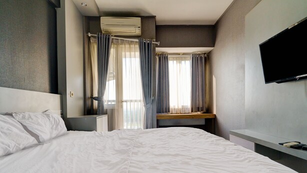 A hotel room with a large bed, a bedside table, a TV mounted on the wall, and a window with curtains. - OYO Life 92889 Apartement Grand Sentraland Karawang By A.t Room (Karawang)