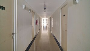 A long, narrow hotel corridor with doors numbered 11 to 22, a fire extinguisher mounted on the wall, and a ceiling-mounted light fixture. - OYO Life 92889 Apartement Grand Sentraland Karawang By A.t Room (Karawang)