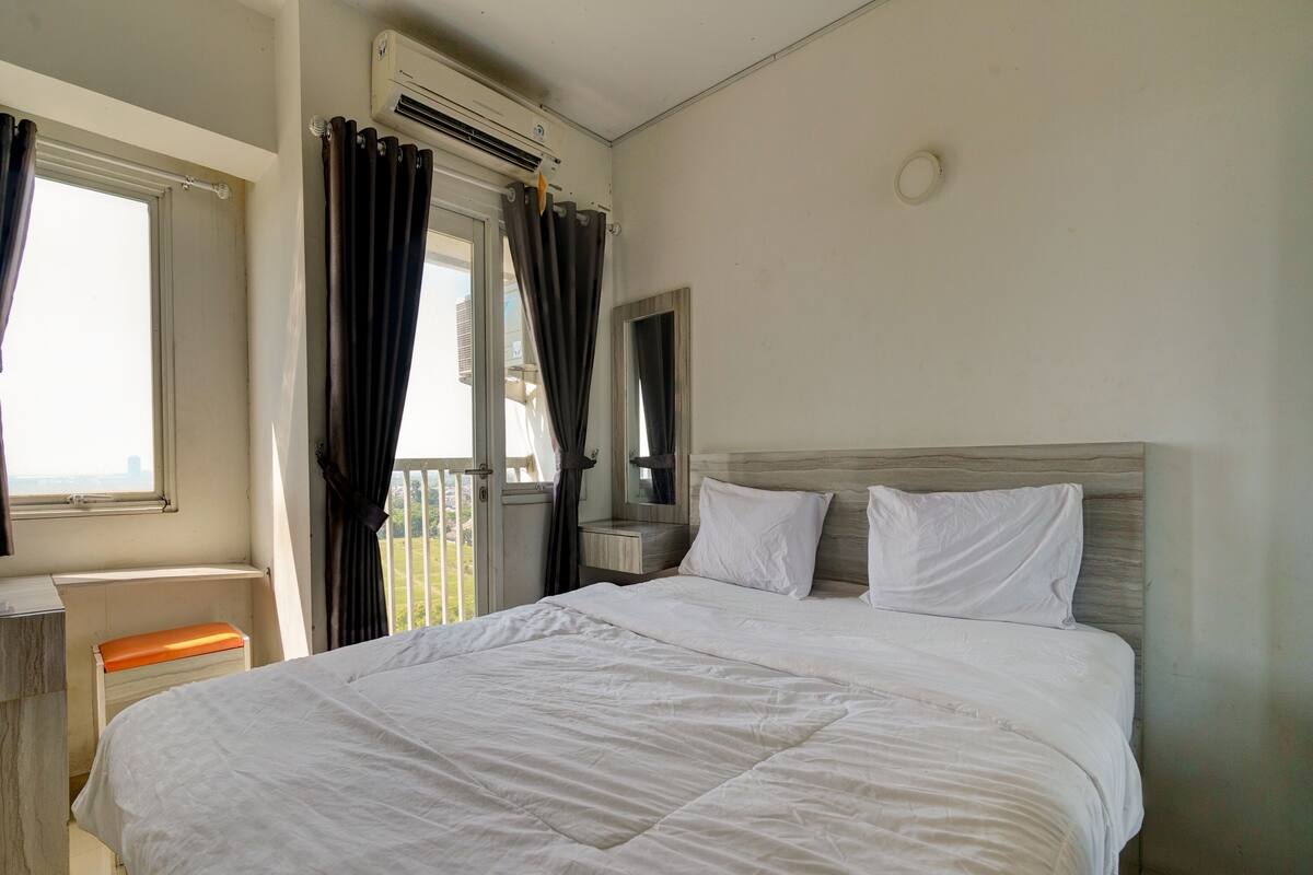 A hotel room with a large bed, a bedside table, a mirror, and a window with curtains.