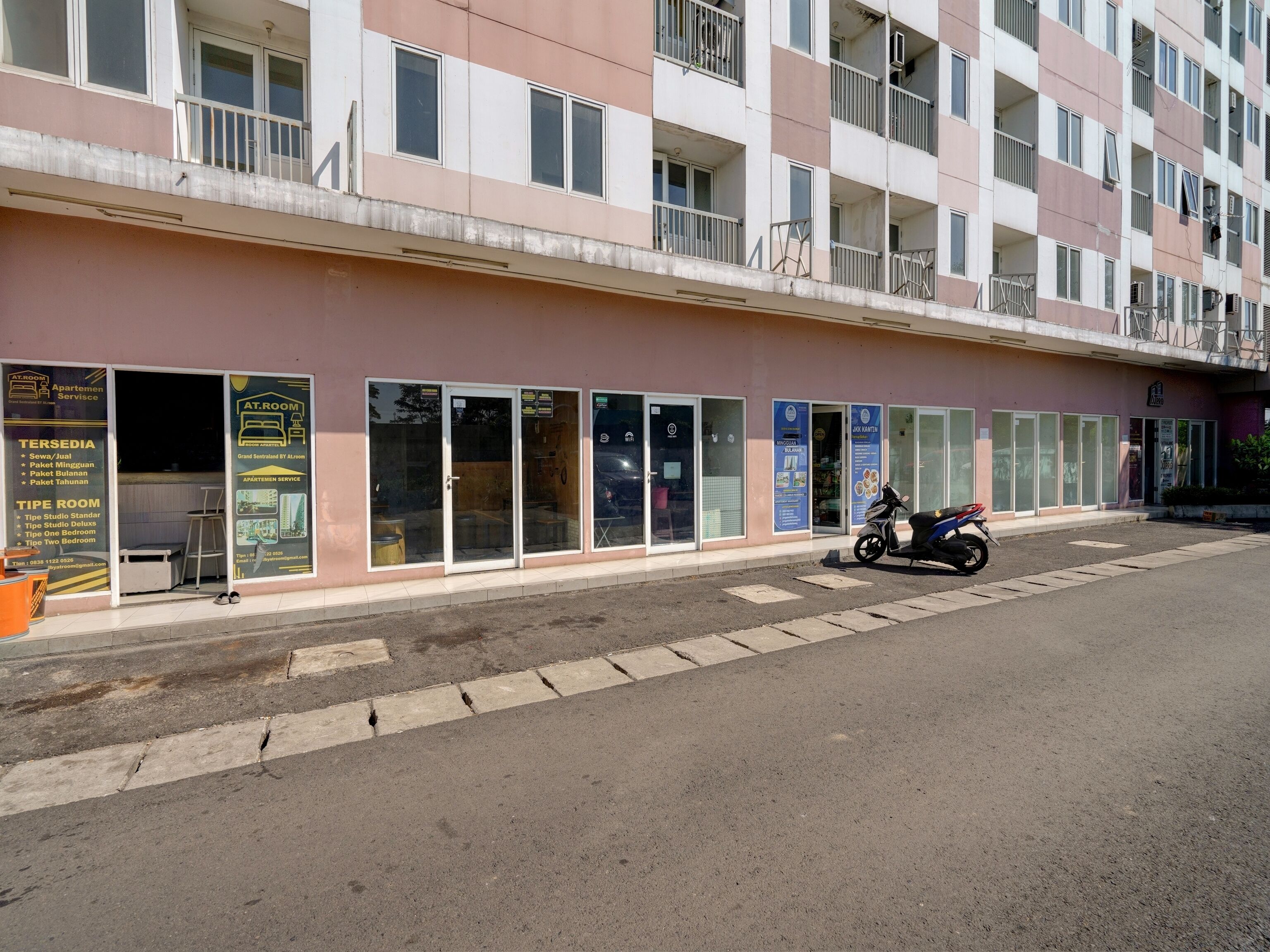 A multi-story building with a row of glass doors and windows, a parked motorcycle, and a sidewalk.